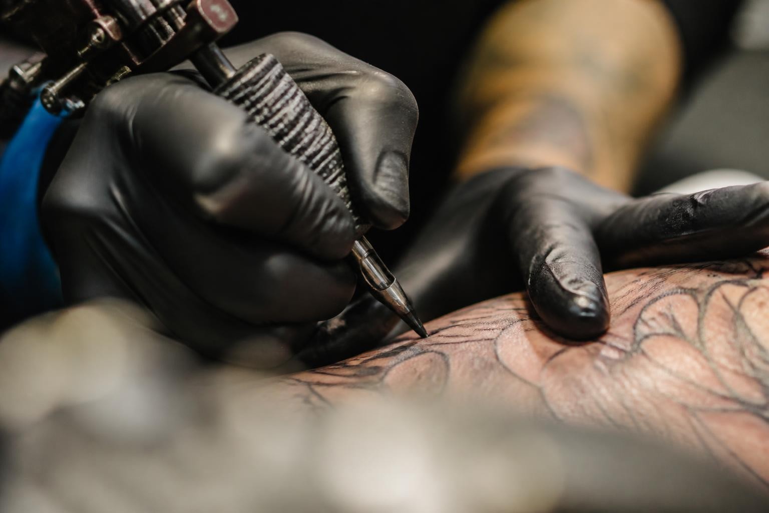 Tatuador finalizando um trabalho em traço fino, fotografado de perto
